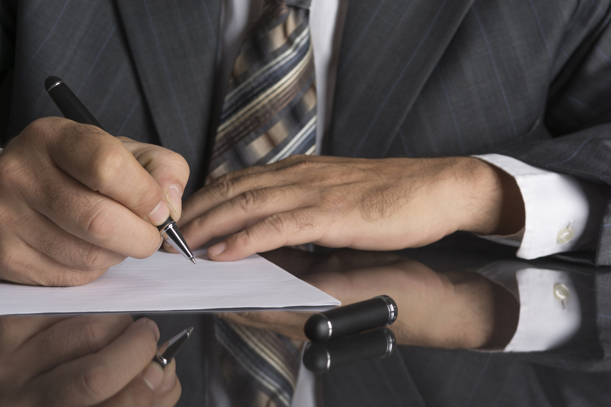 Man in gray suit holds a metal pen and is ready to write on a sheet of paper